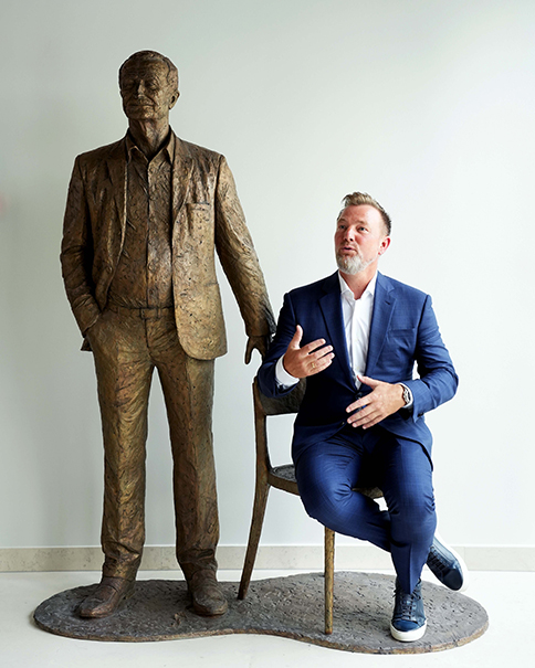 Jacob Brunsborg sentado junto a la figura en bronce de Lars Larsen