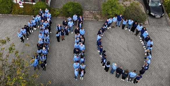 Zahlreiche Menschen in JYSK-Arbeitskleidung bilden gemeinsam eine 110. Das Foto ist in Vogelperspektive aufgenommen