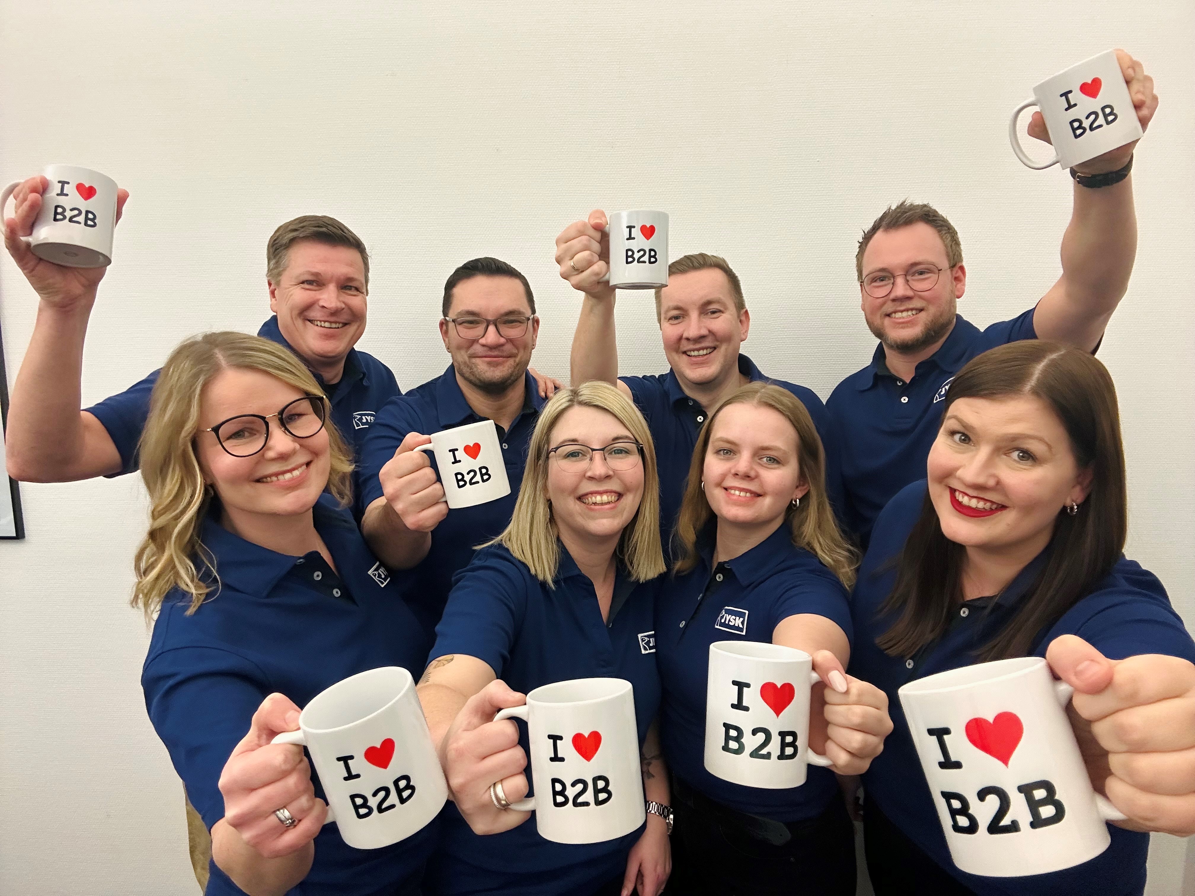 Eight persons in JYSK shirts smile and hold cups with the phrase "I love B2B"