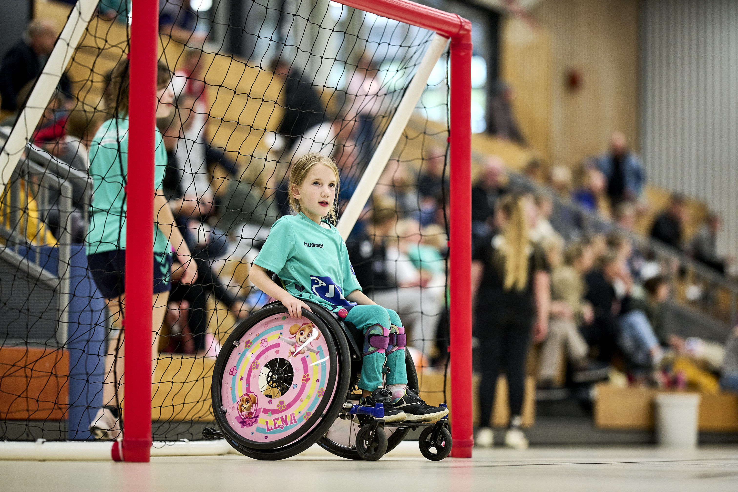 Ein Mädchen sitzt im Rollstuhl, der wiederum in einem Handballtor steht