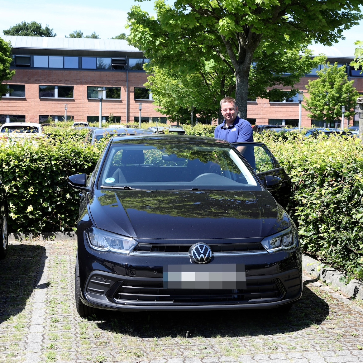 Ein Mann mit kurzen Haaren und JYSK-Poloshirt steht neben einem VW Polo