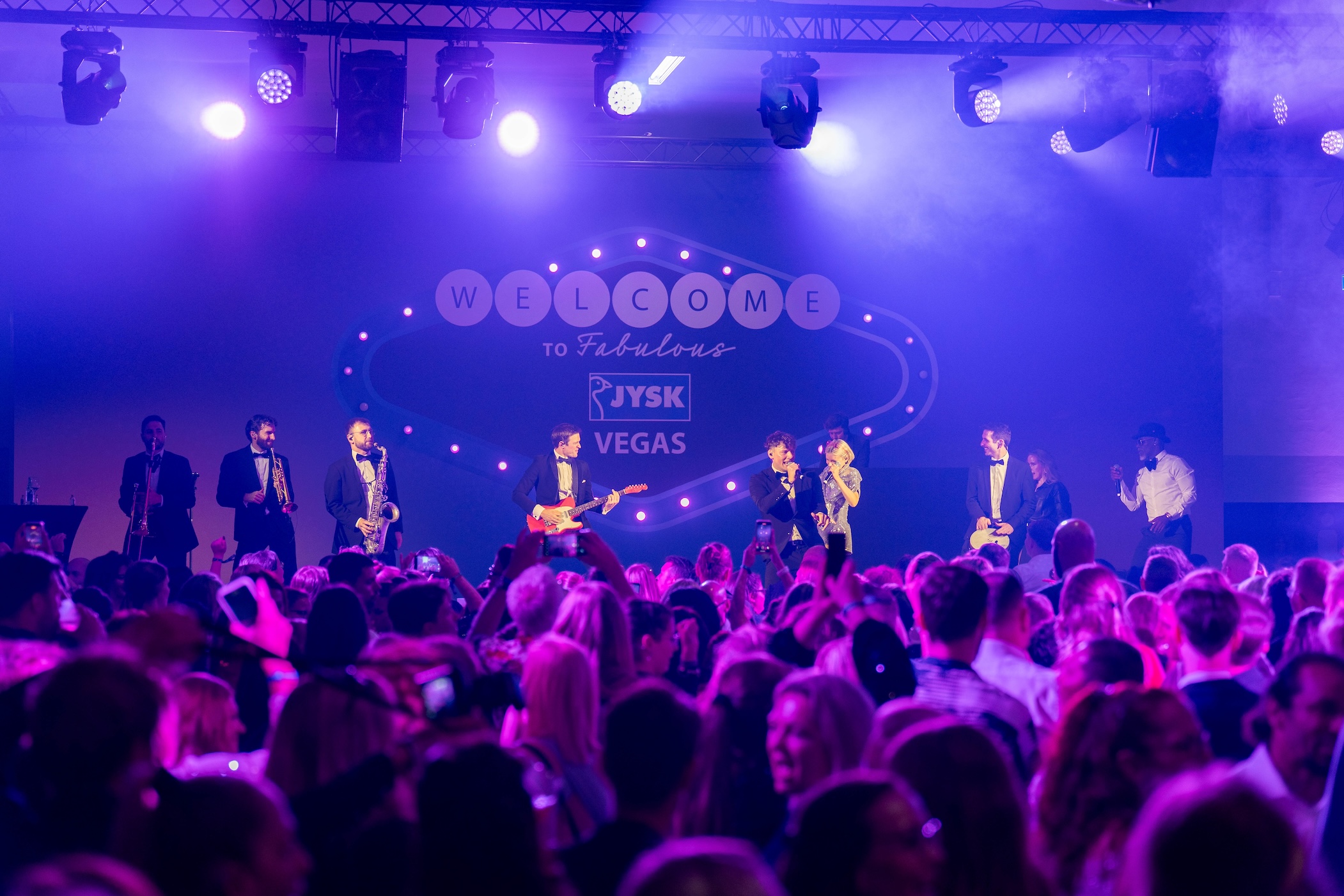 Eine Band steht auf der Bühne. Davor tanzen und stehen zahlreiche Menschen