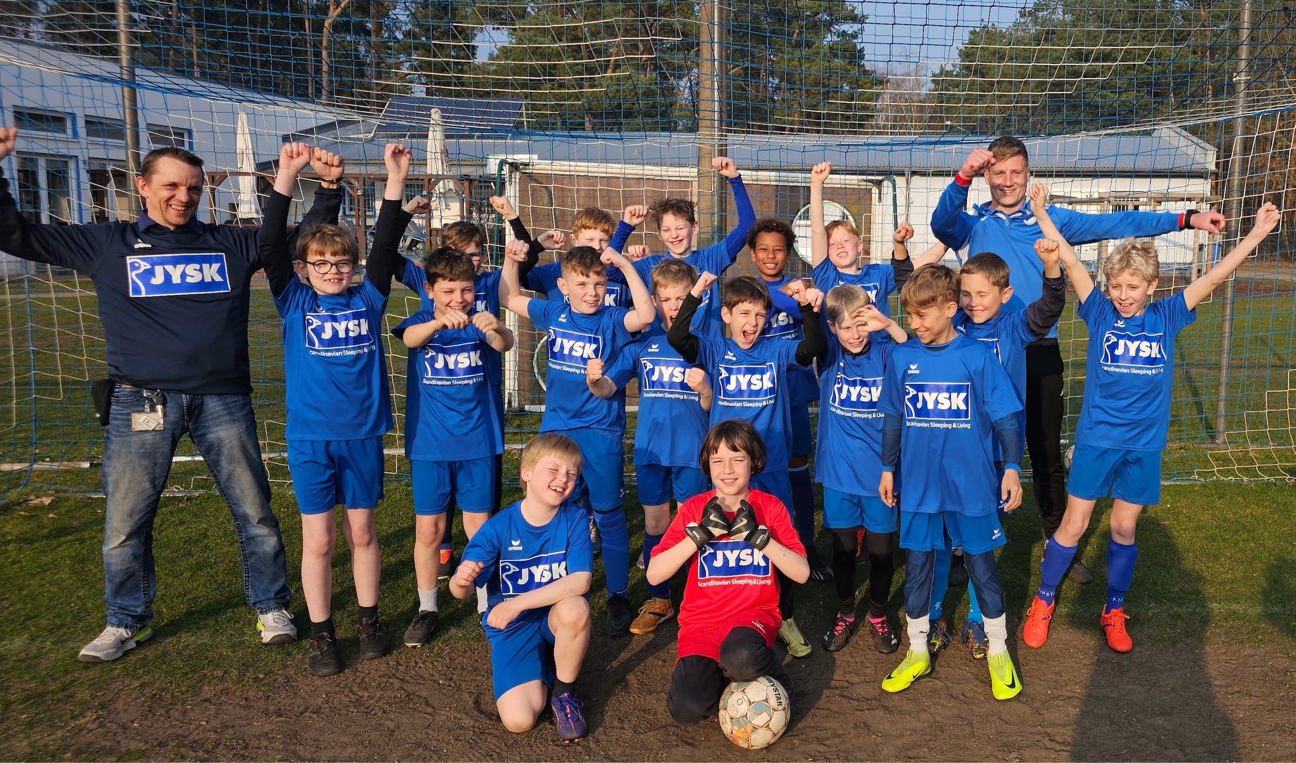Viele Kinder und zwei Erwachsene stehen in einem Fußballtor und jubeln in die Kamera
