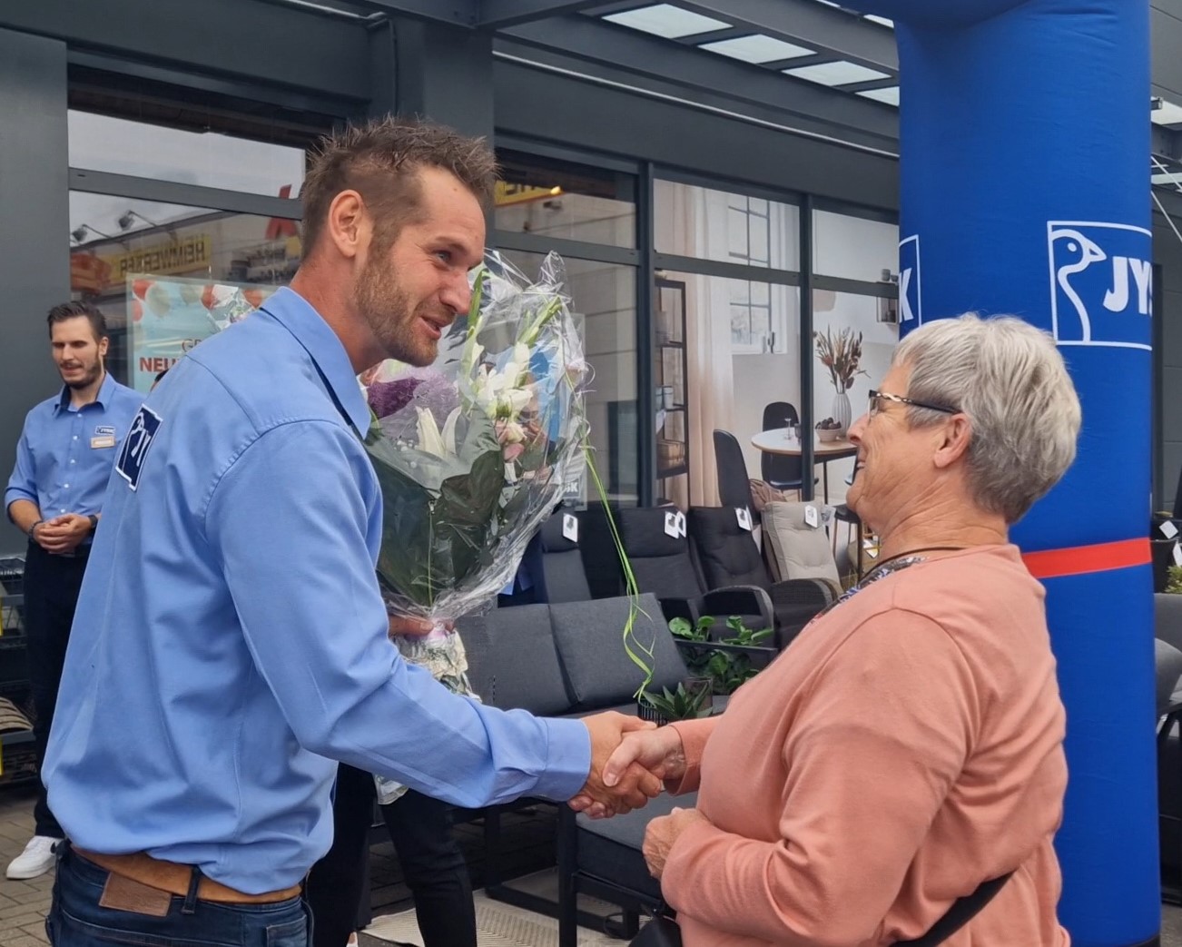 Ein Mann in JYSK-Hemd überreicht einer Dame einen großen Blumenstrauß