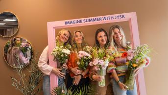 Four women standing with a frame and flowers smiling