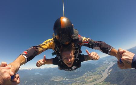A young woman is skydiving. She smiles into the camera and shows thumbs up