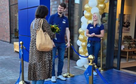 Ein Mann und eine Frau in JYSK-Arbeitskleidung überreichen einer weiteren Frau einen Blumenstrauß