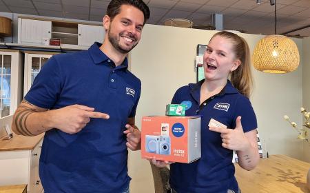 Ein Mann und eine Frau in Poloshirts stehen im Store. Die Frau hält einen Karton in der Hand. Der Mann und die Frau zeigen jeweils mit einem Finger auf diesen Karton. 