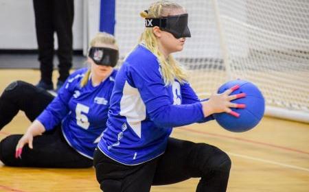 Jasmin Mikkola pelaamassa maalipalloa, keskittyen pallon heittoon joukkuetoveri taustalla.