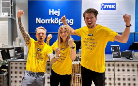 Three Swedish employees with yellow shirts in a JYSK store, cheering on the Swedish team in Paris.