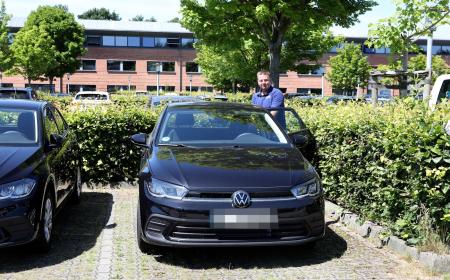 Ein Mann mit kurzen Haaren und JYSK-Poloshirt steht neben einem VW Polo