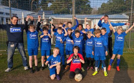 Viele Kinder und zwei Erwachsene stehen in einem Fußballtor und jubeln
